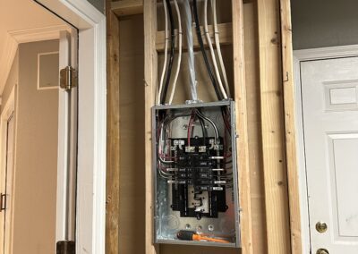 Electrical panel with several wires exposed in an unfinished wall next to a door.