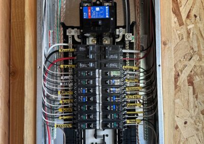 Close-up of an open electrical panel with multiple circuit breakers, various colored wires connected, and labels for identification.